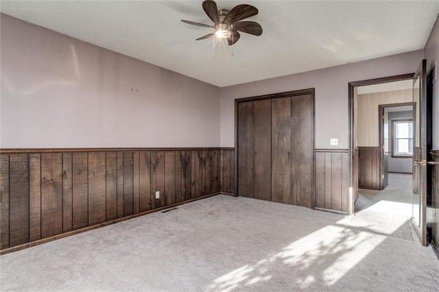 unfurnished bedroom featuring wooden walls, visible vents, a wainscoted wall, carpet floors, and a closet