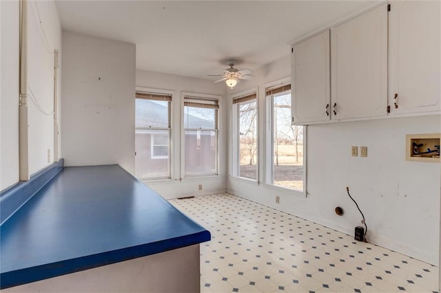 interior space with baseboards, light floors, white cabinetry, and a ceiling fan