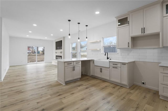 kitchen with a healthy amount of sunlight, a peninsula, light wood-style flooring, a sink, and tasteful backsplash