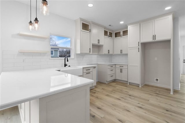 kitchen featuring tasteful backsplash, glass insert cabinets, a peninsula, hanging light fixtures, and a sink