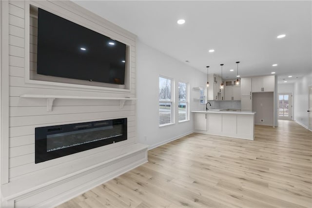 unfurnished living room featuring recessed lighting, light wood-style flooring, a fireplace, and a sink