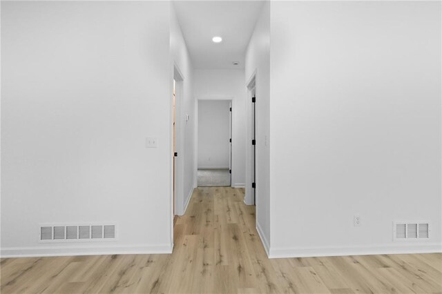 hallway featuring visible vents, light wood-style flooring, and baseboards