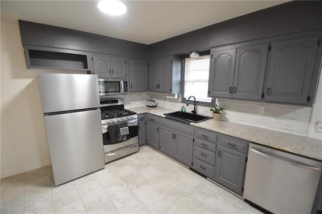 kitchen featuring backsplash, appliances with stainless steel finishes, gray cabinets, and a sink