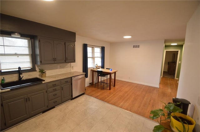 kitchen featuring baseboards, visible vents, gray cabinetry, stainless steel dishwasher, and a sink