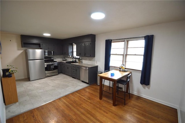 kitchen with light countertops, appliances with stainless steel finishes, a sink, light wood-type flooring, and baseboards