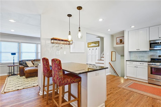 kitchen with light wood finished floors, decorative backsplash, appliances with stainless steel finishes, and white cabinetry