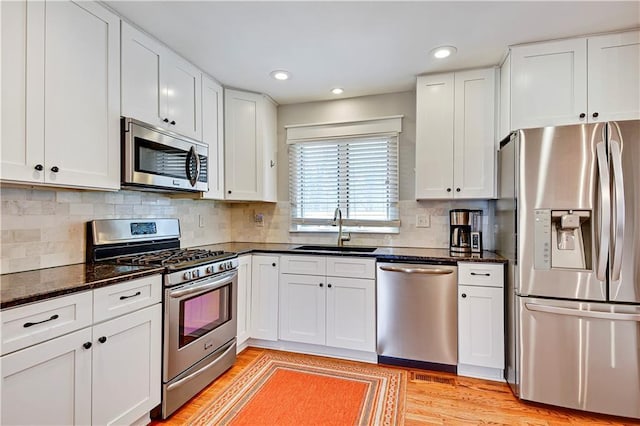 kitchen with light wood finished floors, tasteful backsplash, appliances with stainless steel finishes, white cabinets, and a sink