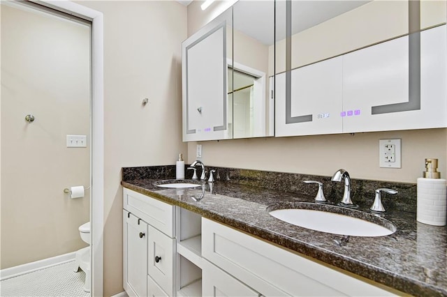 bathroom featuring double vanity, toilet, baseboards, and a sink