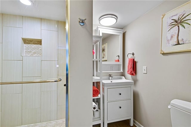 bathroom featuring vanity, toilet, baseboards, and a tile shower