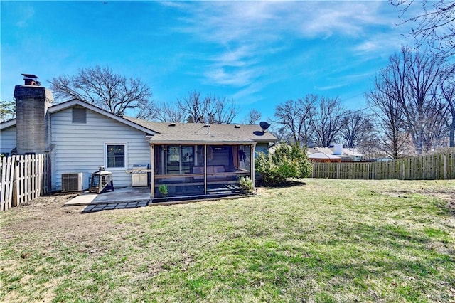 rear view of property featuring a lawn, a patio, a fenced backyard, a sunroom, and a chimney