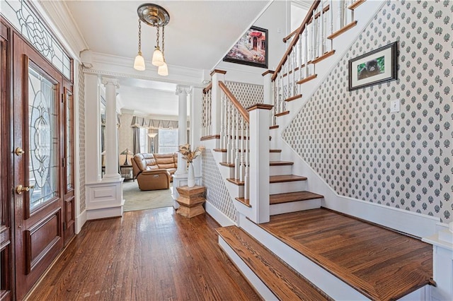 entryway featuring ornamental molding, wood finished floors, stairway, wallpapered walls, and ornate columns