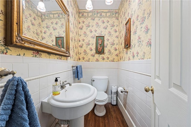 half bathroom featuring a wainscoted wall, toilet, wood finished floors, and wallpapered walls