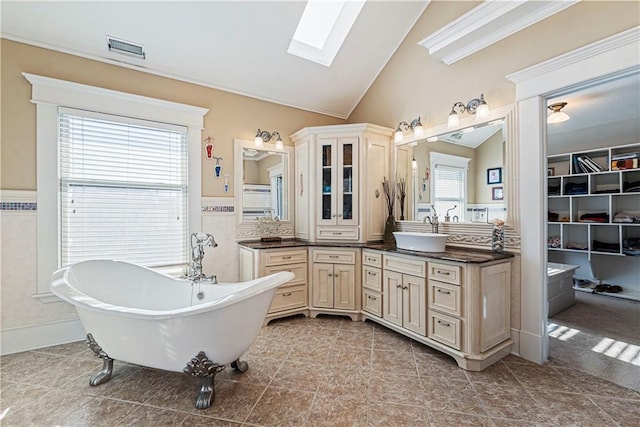 bathroom with a freestanding tub, visible vents, lofted ceiling with skylight, wainscoting, and vanity