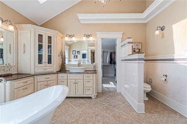 bathroom featuring a wainscoted wall, toilet, a soaking tub, vanity, and vaulted ceiling