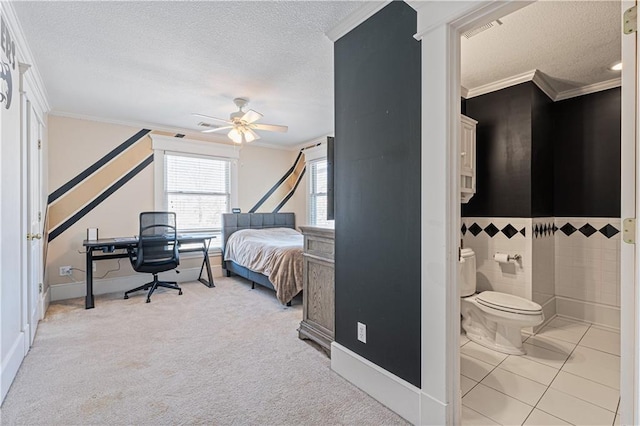 carpeted bedroom featuring ceiling fan, ornamental molding, ensuite bathroom, a textured ceiling, and tile walls