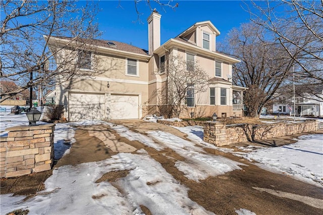 american foursquare style home with stucco siding, an attached garage, a chimney, and driveway