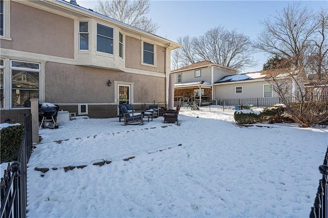 snow covered rear of property with stucco siding, an outdoor hangout area, and fence