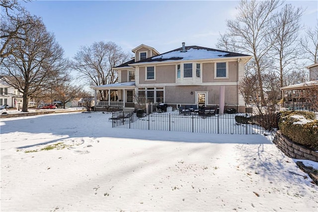 snow covered house with a fenced front yard, covered porch, and stucco siding