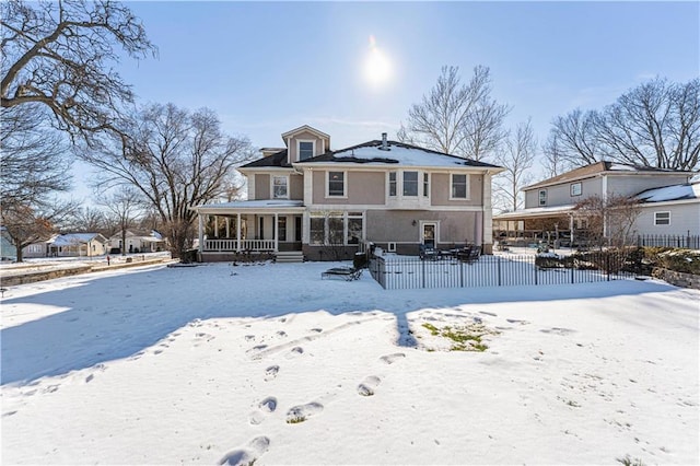 snow covered rear of property with a porch and fence