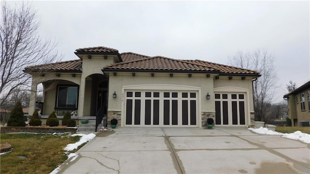 mediterranean / spanish home featuring a tile roof, stucco siding, driveway, stone siding, and an attached garage