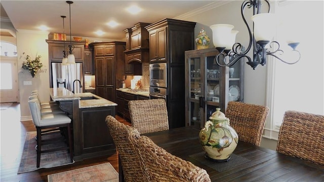 kitchen with a center island with sink, dark wood finished floors, ornamental molding, appliances with stainless steel finishes, and decorative light fixtures