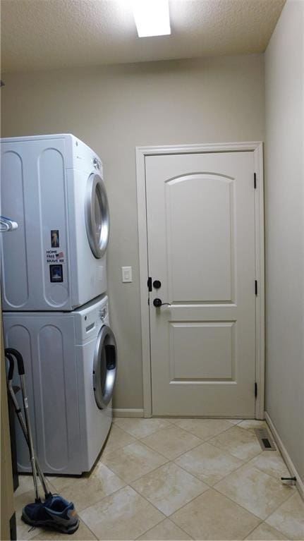 washroom with stacked washer / dryer, baseboards, light tile patterned floors, laundry area, and a textured ceiling