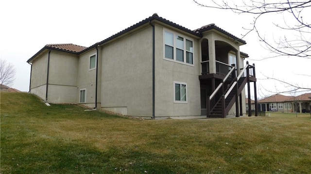 rear view of property with stairway, a yard, stucco siding, and a tiled roof