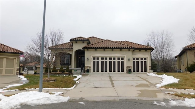 mediterranean / spanish house with stucco siding, concrete driveway, a garage, stone siding, and a tile roof