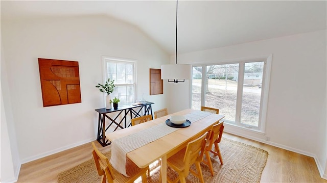 dining area with light wood-style floors, vaulted ceiling, and baseboards