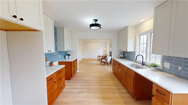 kitchen with light wood-type flooring, tasteful backsplash, brown cabinetry, and a sink