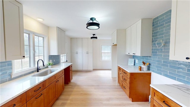 kitchen with light stone countertops, decorative backsplash, brown cabinets, and a sink