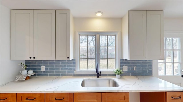 kitchen with light stone counters, a sink, and backsplash