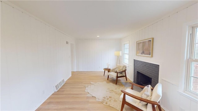 living area featuring a brick fireplace, light wood-style flooring, and visible vents