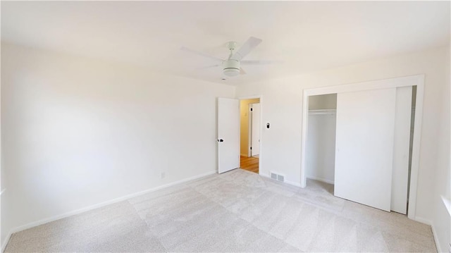 unfurnished bedroom with a closet, light colored carpet, visible vents, ceiling fan, and baseboards