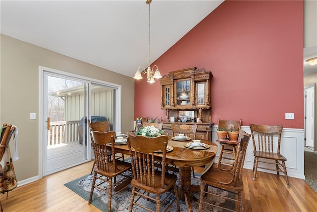 dining space with a notable chandelier, high vaulted ceiling, light wood-type flooring, and a wainscoted wall