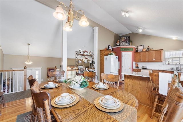 dining space featuring ornate columns, light wood-type flooring, a chandelier, and vaulted ceiling