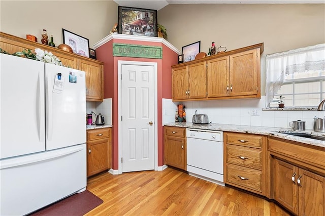 kitchen with a sink, white appliances, tasteful backsplash, and brown cabinetry