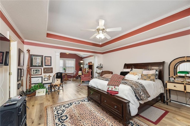 bedroom featuring ornate columns, light wood-style flooring, ceiling fan, ornamental molding, and a raised ceiling