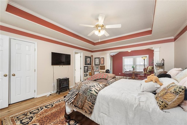 bedroom featuring baseboards, ornate columns, crown molding, light wood-style floors, and a raised ceiling