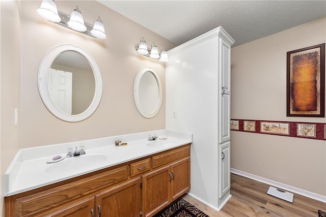 full bathroom with a sink, a textured ceiling, wood finished floors, and double vanity