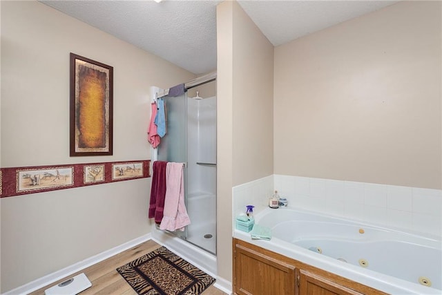 full bath with wood finished floors, baseboards, a tub with jets, a shower stall, and a textured ceiling