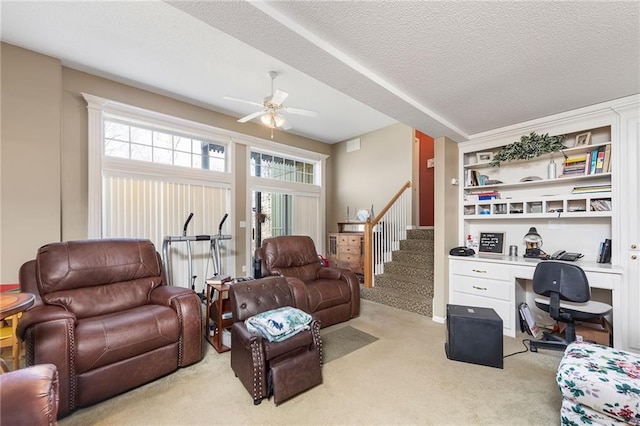 living area featuring a textured ceiling, ceiling fan, stairs, built in desk, and light carpet