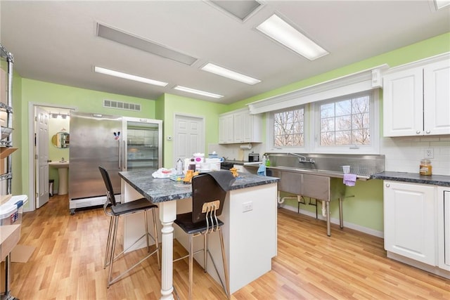 kitchen featuring visible vents, light wood-style floors, a breakfast bar area, and white cabinetry