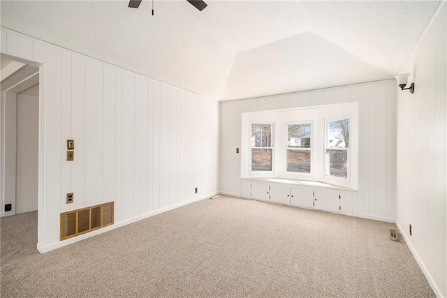 empty room with visible vents, carpet, a ceiling fan, and vaulted ceiling