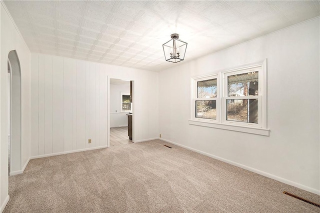 empty room featuring baseboards, light colored carpet, visible vents, and a chandelier