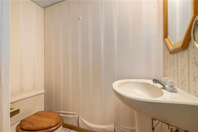 bathroom featuring a sink, toilet, and wallpapered walls