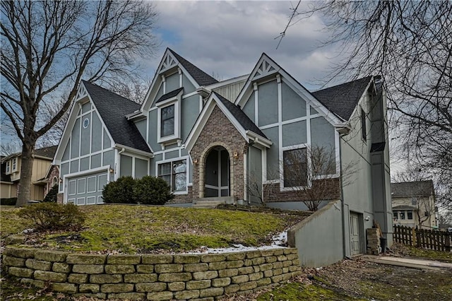 tudor house featuring brick siding, roof with shingles, fence, and stucco siding