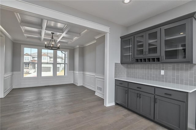 kitchen with a notable chandelier, gray cabinetry, wood finished floors, glass insert cabinets, and crown molding