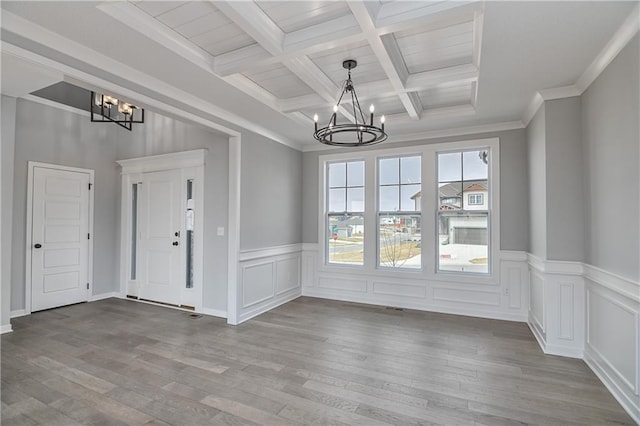 interior space with ornamental molding, wood finished floors, beam ceiling, and an inviting chandelier