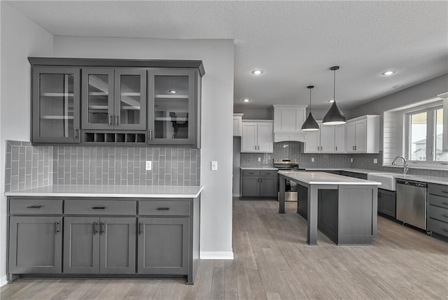 kitchen with stainless steel appliances, a sink, light wood-type flooring, gray cabinets, and glass insert cabinets